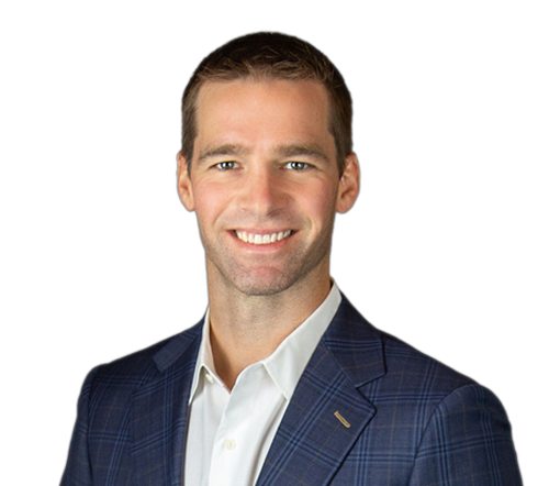 A man with short brown hair, wearing a blue plaid suit jacket and white shirt, smiling at the camera against a plain light background.