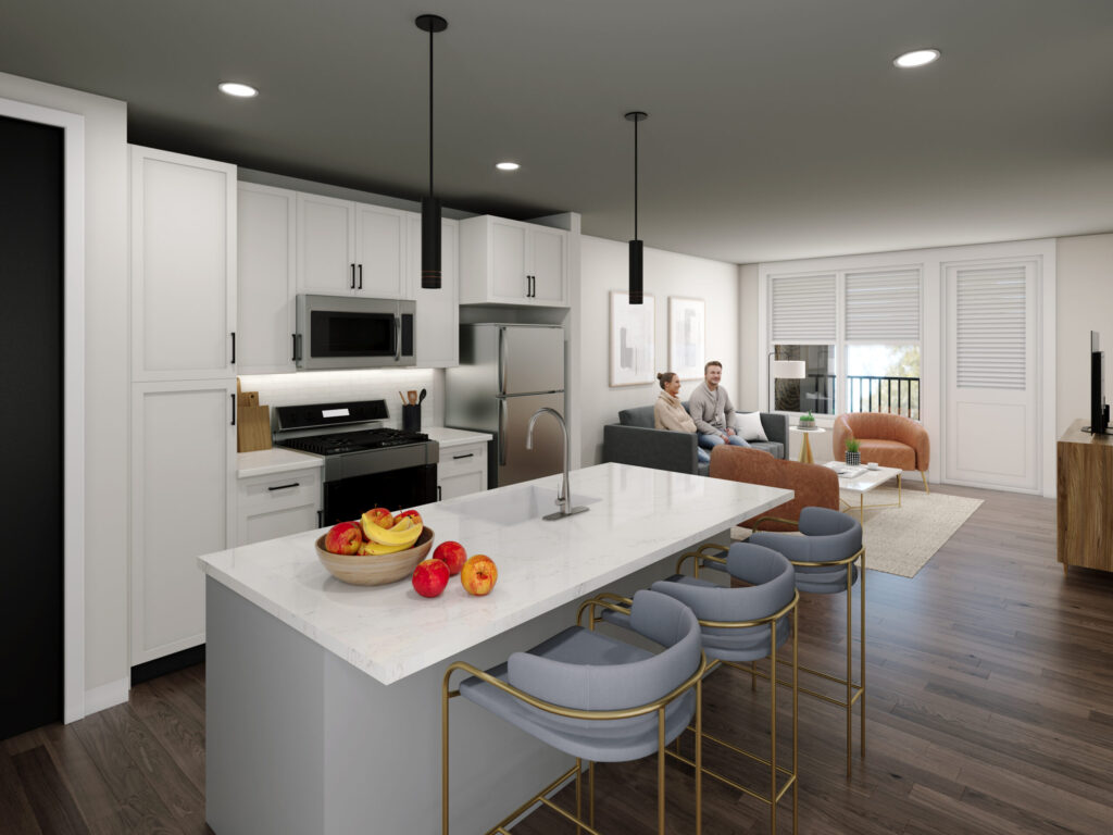 Modern kitchen with white cabinets, stainless steel appliances, and a marble island with fruit bowls and barstools. In the background, two people sit on a couch in a bright living room with large windows.